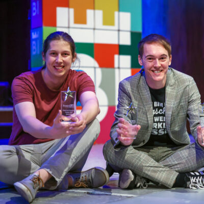 Die Preistragenden des diesjährigen FameLab-Deutschlandfinales sitzen auf der Bühne und zeigen ihre Preise: Dr. Christian Scharun (rechts) und Niklas Hoffmann.