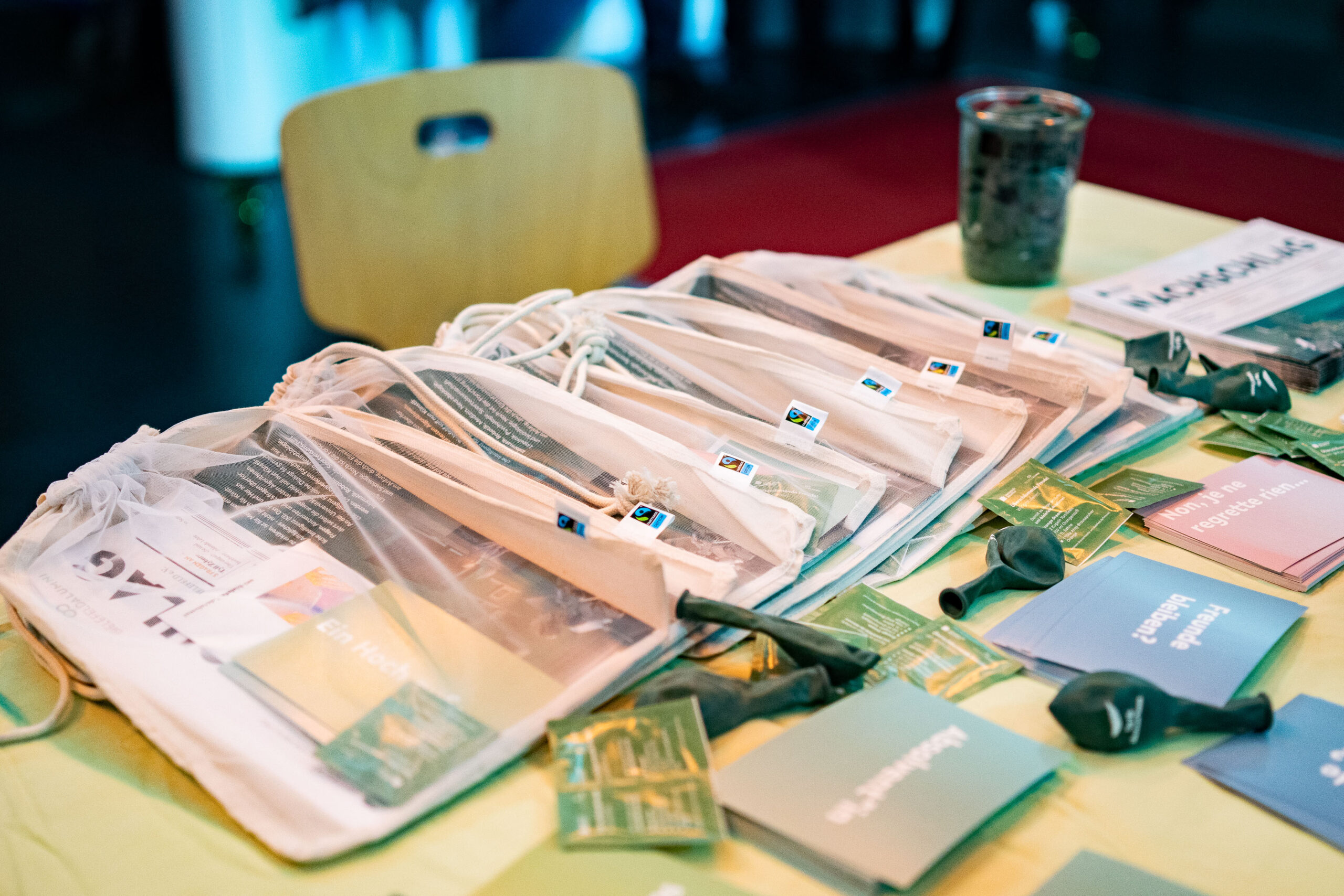 Tag für Absolvent:innen: Auf einem Tisch am Stand des Absolvent Netzwerks liegen kleine Geschenke für alle Absolvent:innen aus: Brötchentüten, Postkarten, Luftballons und Brausepäckchen.