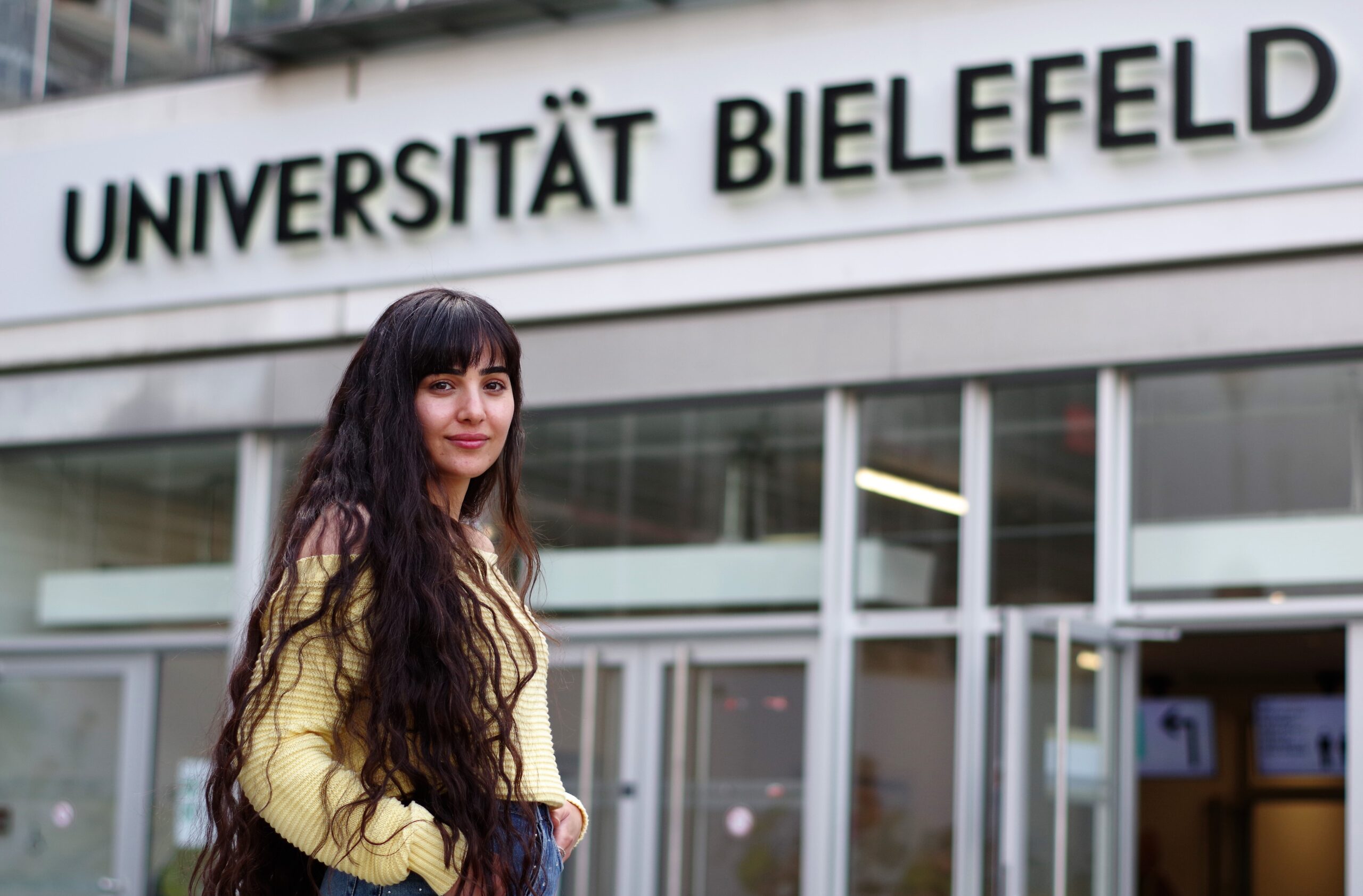 Foto von Ahin Hassaf vor dem Haupteingang der Uni Bielefeld.