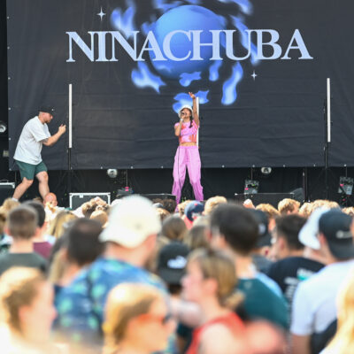 Nina Chuba singt auf der Hauptbühne in ihr Mikrofon. Im Vordergrund sind verschwommen Festivalbesucher*innen.