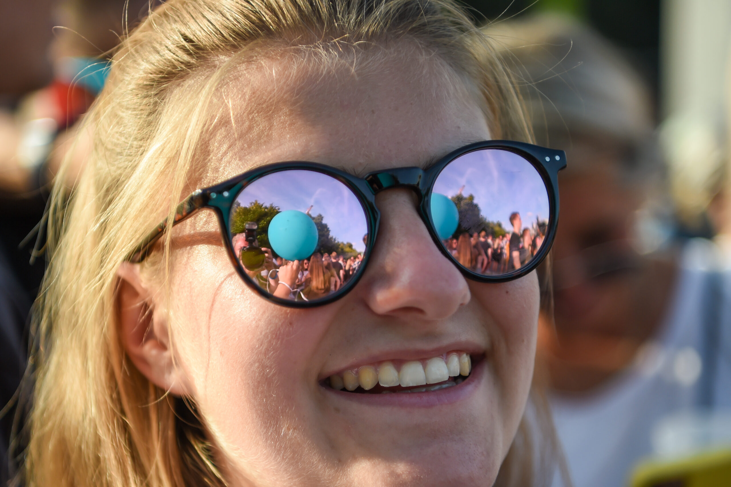 Frau mit Sonnenbrille, in der sich das Festival spiegelt.