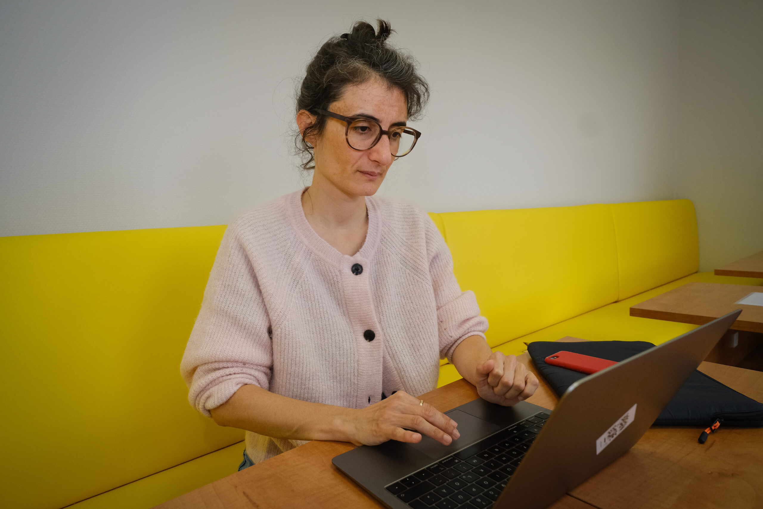 Die Philosophie-Professorin Christine Bratu sitzt auf einer gelben Bank und arbeitet am Laptop.