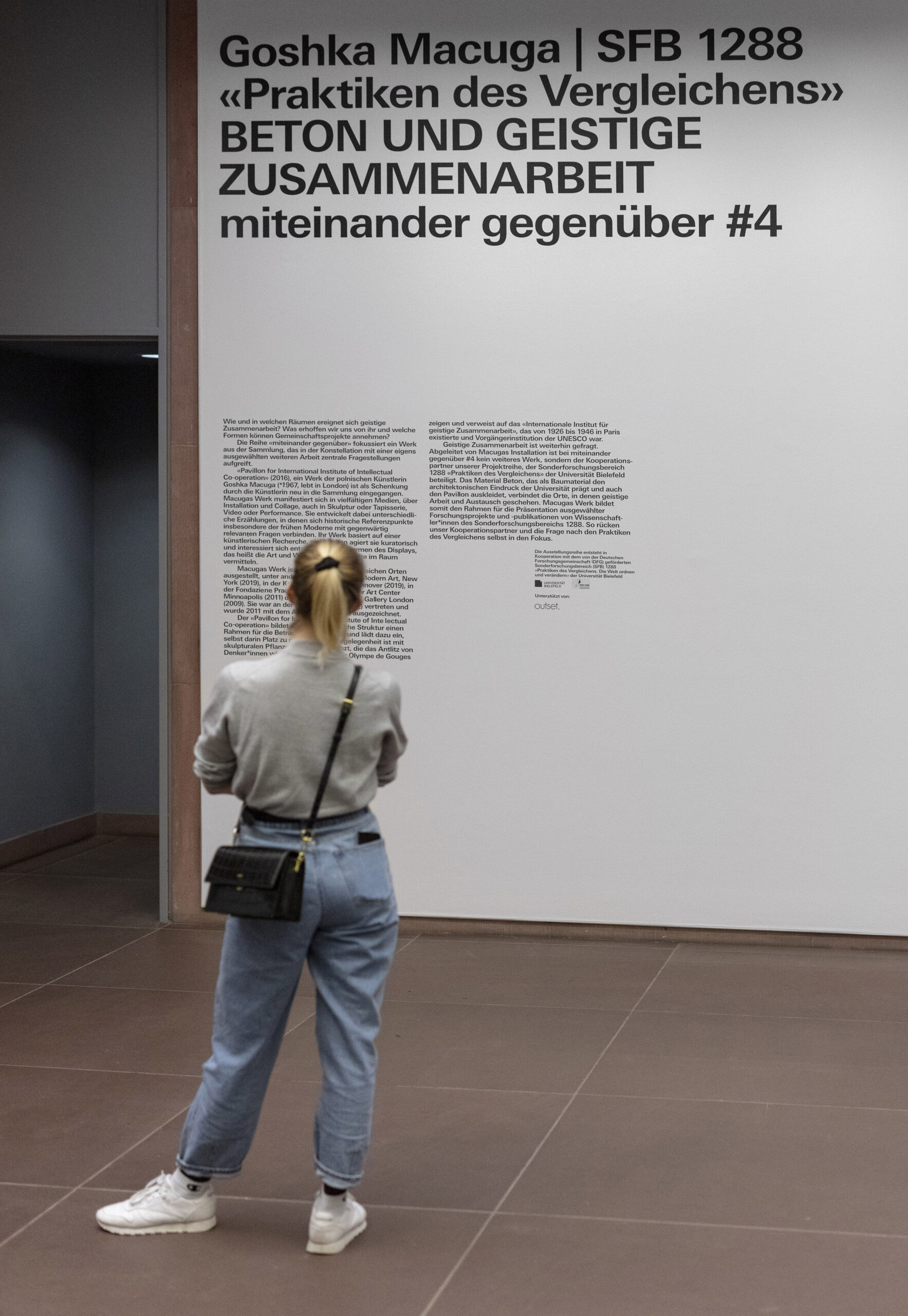 Eine Person steht vor einer Wand mit Text darauf.