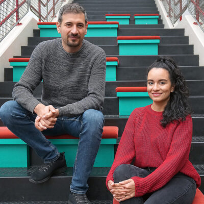 Mustafa Braun und Marcela Feijoo Gomez sitzen auf einer Treppe.
