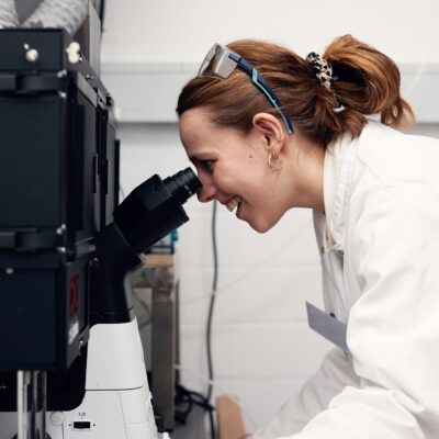 Junge Frau schaut durch ein Mikroskop.