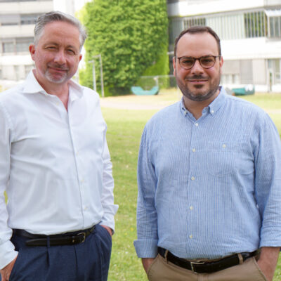 Prof. Dr. Frank Riedel und Prof. Dr. Giorgio Ferrari vor einem Gebäude der Universität Bielefeld.