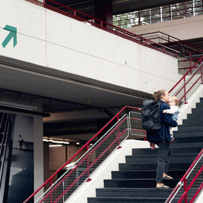 Mann mit Kind auf dem Arm schreitet eine Treppe in der Uni-Halle hoch.