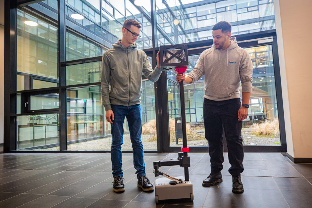 Robot in a foyer with two people touching  it and looking at it