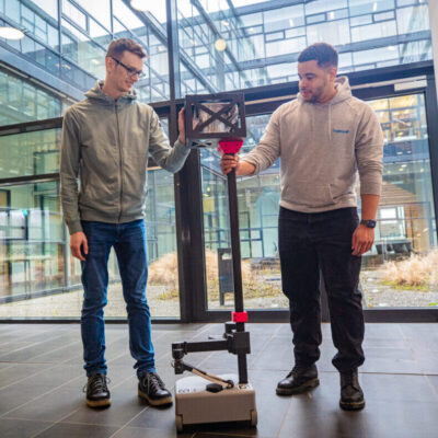 Robot in a foyer with two people touching it and looking at it