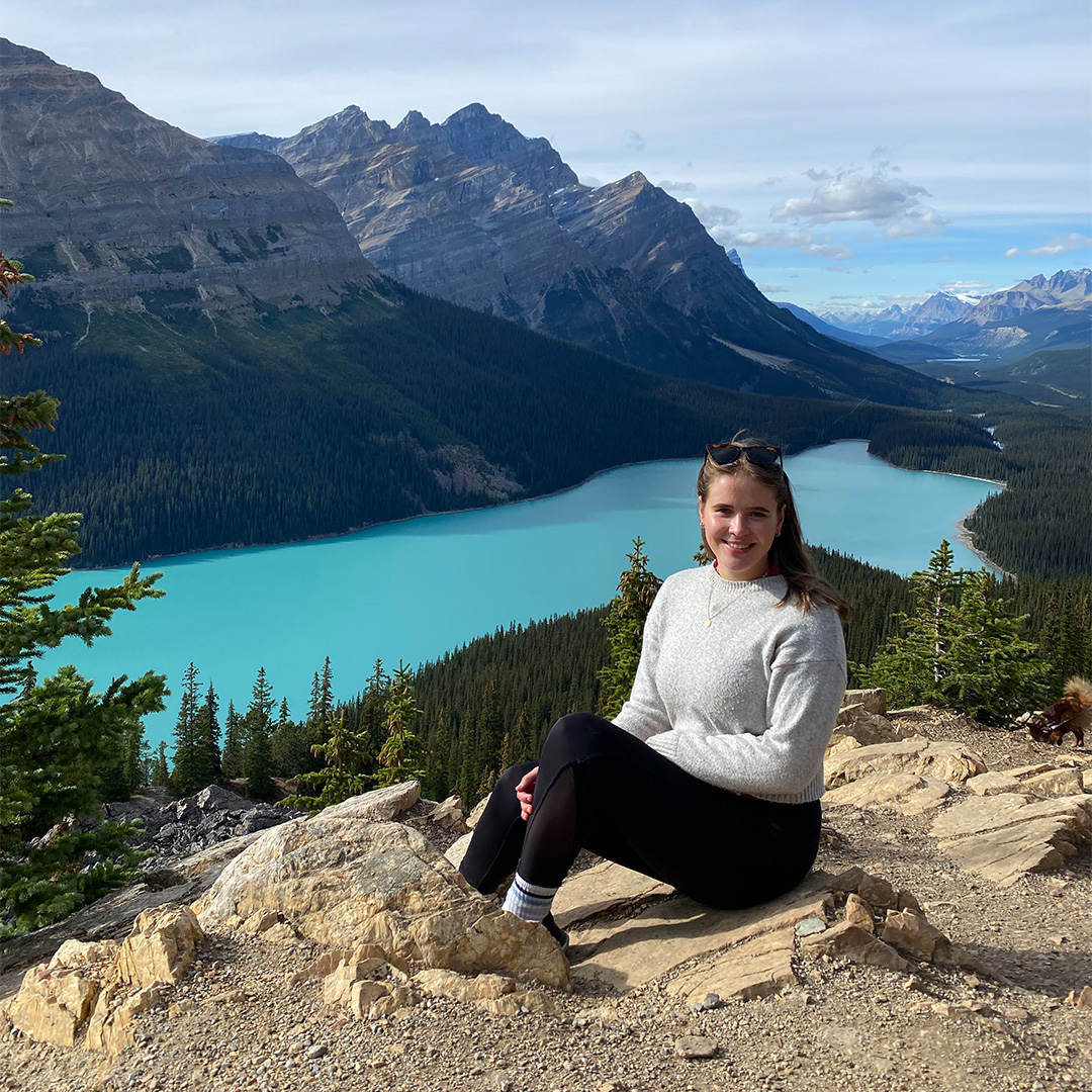 Emelie Gottschling sitting on a rock, with mountains and a lake in the background.