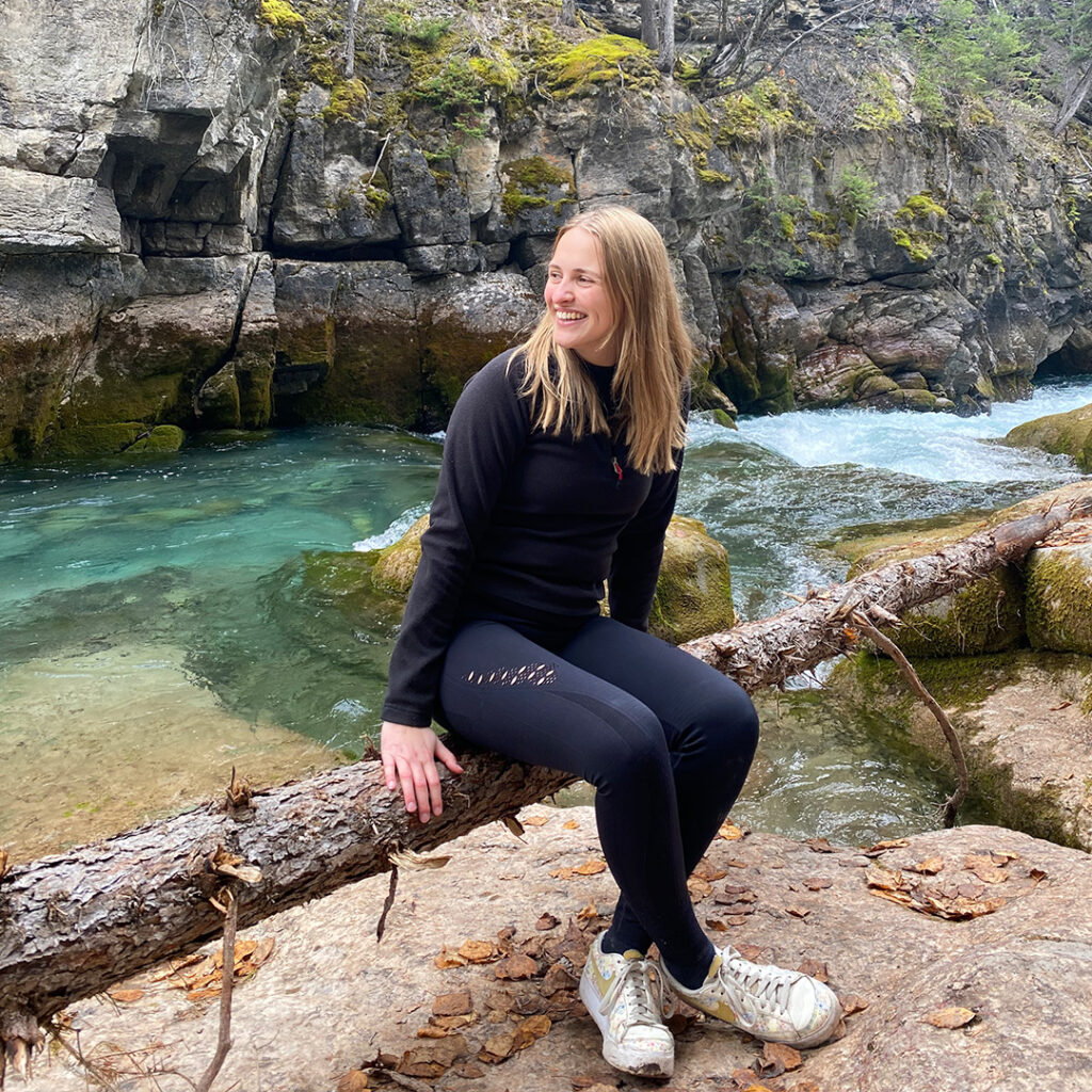 Lilli Sophie Kaimann sitzt auf einem Baumsturz am Flussufer