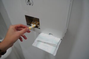 Hand entnimmt Tampon aus einem Spender mit Periodenprodukten.