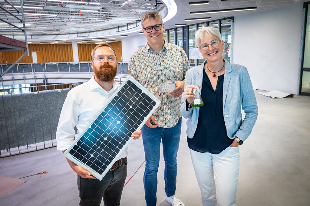 Zwei Männer und eine Frau stehen im Obergeschoss der Wissenswerkstadt, sie halten jeweils Gegenstände, u.a. ein Solarmodul