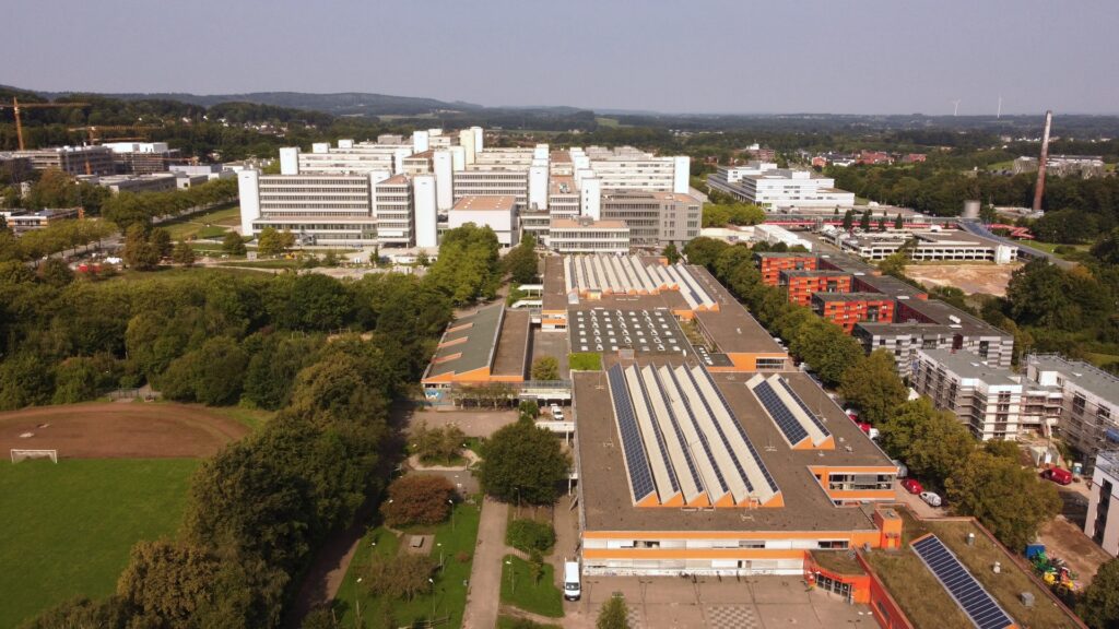 Luftaufnahme mit zwei Schulgebäuden im Vordergrund und dem Universitätshauptgebäude im Hintergrund