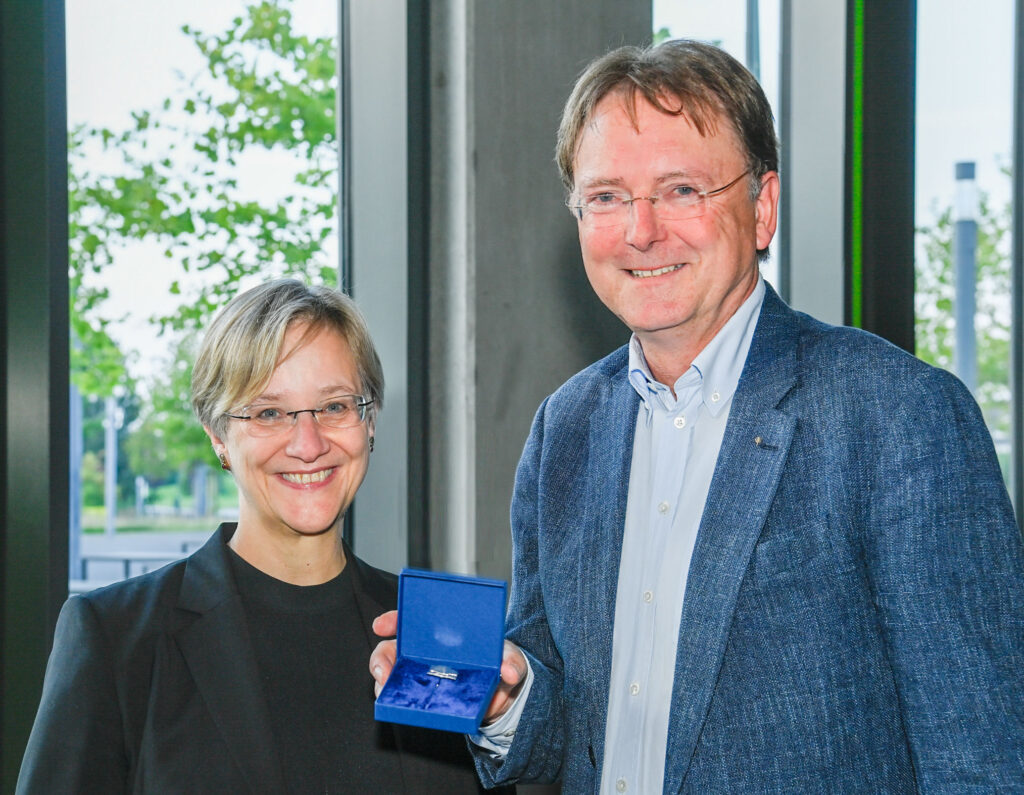 Rektorin Prof. Dr. Angelika Epple, links im Bild und Prof. Dr. Fred Becker, rechts im Bild hält die Ehrennadel der Universität Bielefeld.