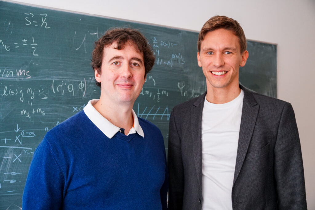 Dr. Bastian Brand und Professor Dr. Sören Schlichting stehen vor einer Tafel mit Formeln.