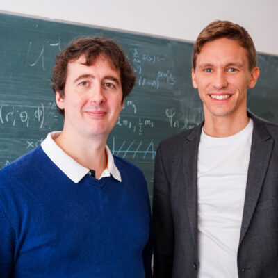 Dr. Bastian Brand und Professor Dr. Sören Schlichting stehen vor einer Tafel mit Formeln.