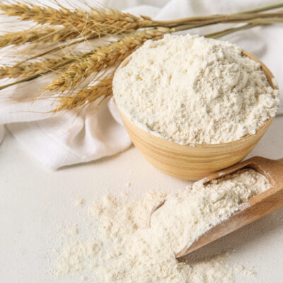 Bowl and scoop with wheat flour on white table