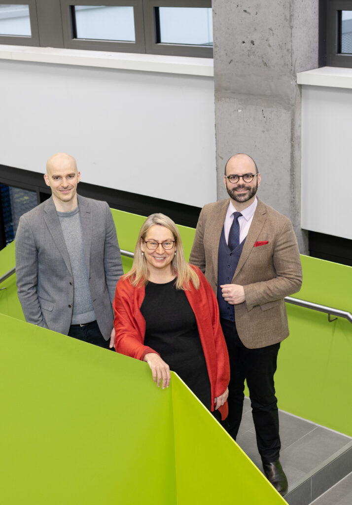 Prof. Dr. Martin Petzke, Prof’in Dr. Antje Flüchter und Prof. Dr. Maximilian Benz stehen auf einer Treppe