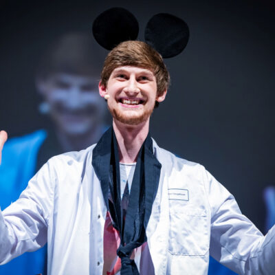 Julian Neugebauer im weißen Kittel auf der FameLab-Bühne