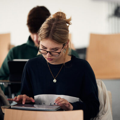 Studentin tippt im Seminarraum auf Tablet.