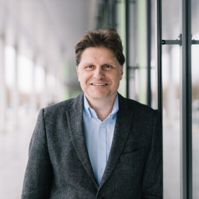 Der Professor vor einer Gebäudefront aus Glas.