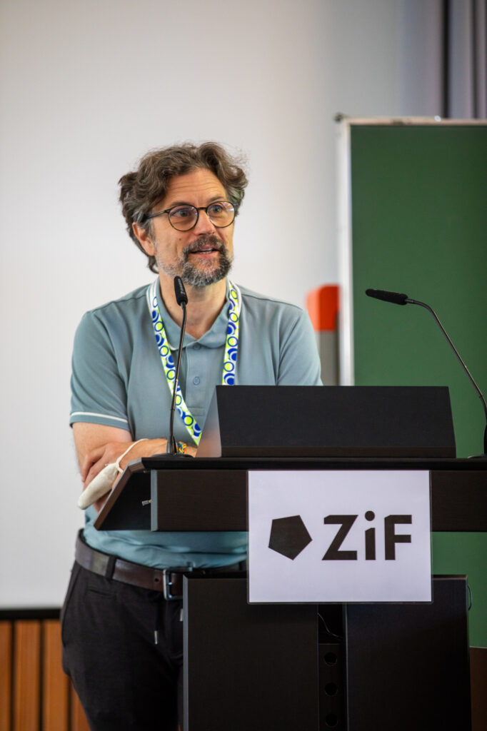 Ein Mann in grauem T-Shirt hinter einem Rednerpult mit der Aufschrift ZiF.