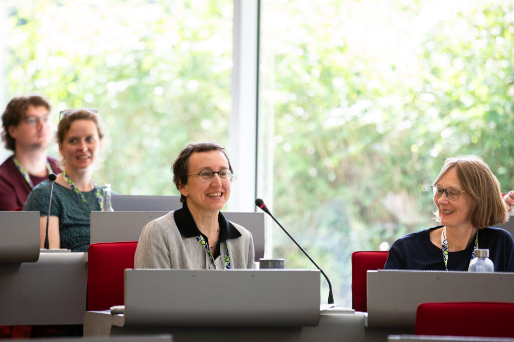Eine Frau in einem Konferenzsaal mit Mikrofon, sitzend.