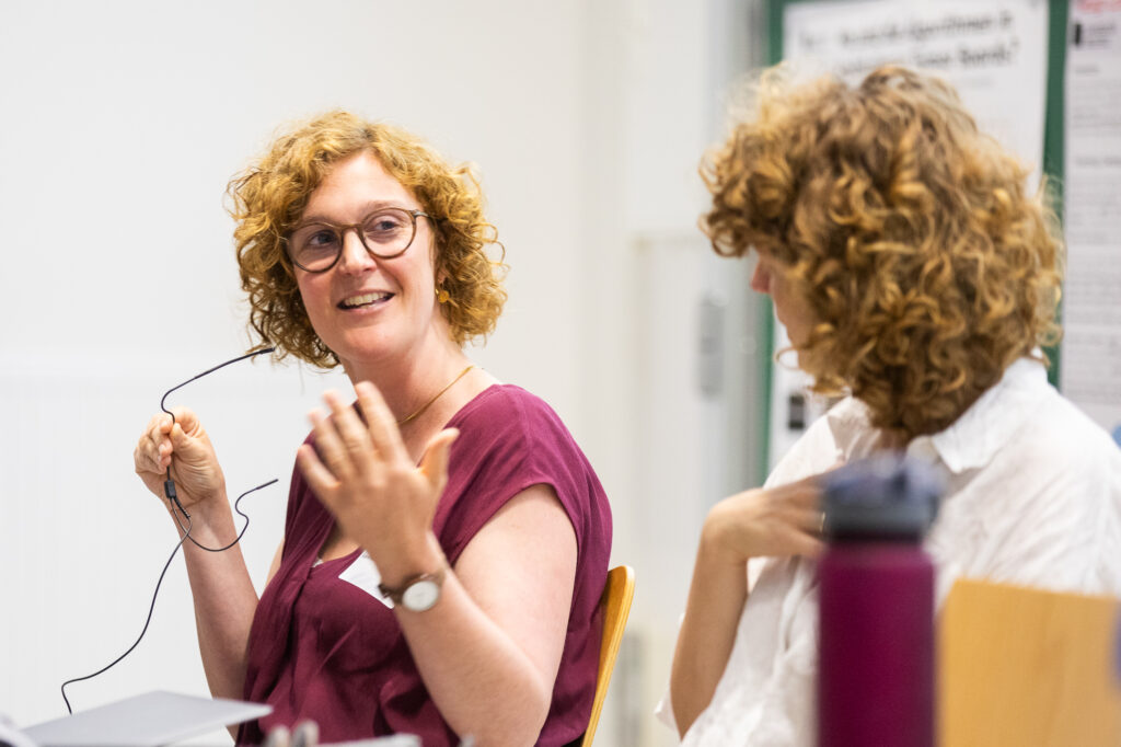 Frau mit Locken in einem roten T-Shirt gekleidet mit Mikrophon und erklärender Handhaltung