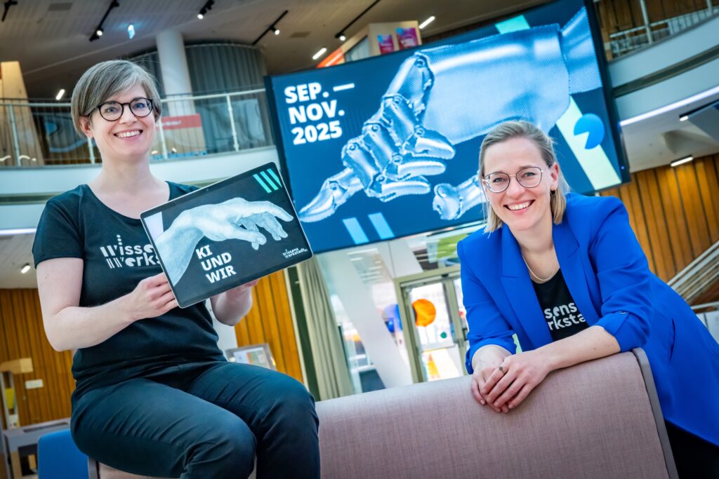 Projektleiterin Maria Munzert (l.) und Gesa Fischer(r.) haben ein Tablete im Hand und darauf steht ' KI und wir'