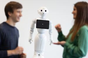 Zwei Personen, ein Mann und eine Frau, unterhalten sich vor einem Roboter.