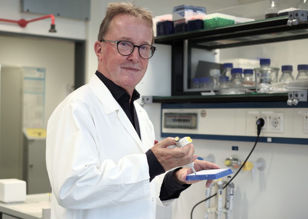 Professor Dr. Jörn Kalinowski im Laborkittel verwendet eine Mikroliterpipette