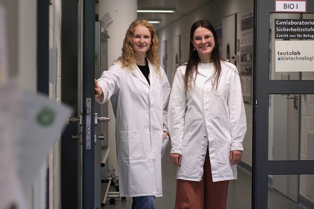 Zwei Studentinnen in Laborkitteln in einem Laborflur