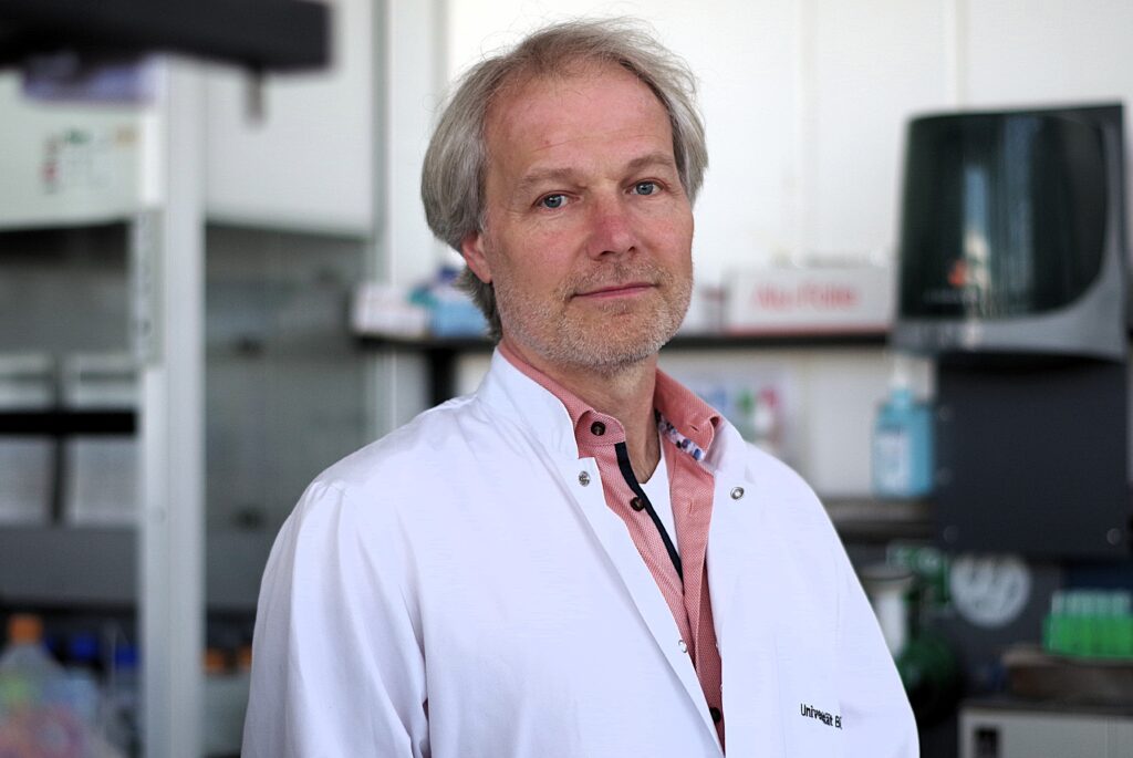 Professor Dr. Kristian Müller im Laborkittel, Labor im Hintergrund