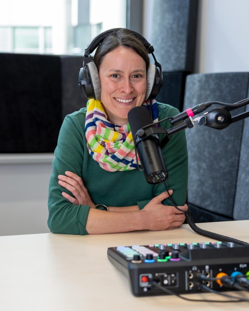 Dr. Anna-Christina Nowak sitzt an einem Tisch, vor sich ein Mikrofon. Im Vordergrund des Bildes ein Mischpult.