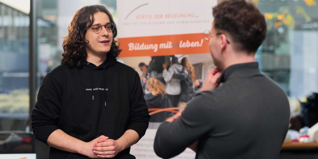 Ein Student mit einem Pulli mit der Aufschrift "Universität Bielefeld" im Kontakt mit einer anderen Person.