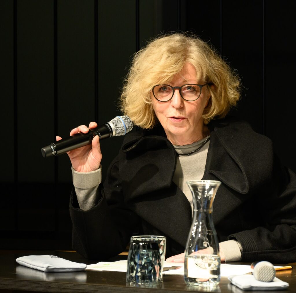 Professorin Dr. Doris Schaeffer vor dunklem Hintergrund, während sie einen Vortrag hält