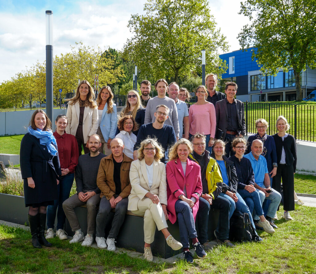 Außenaufnahme der Mitglieder, im Hintergrund Bäume und ein Gebäude