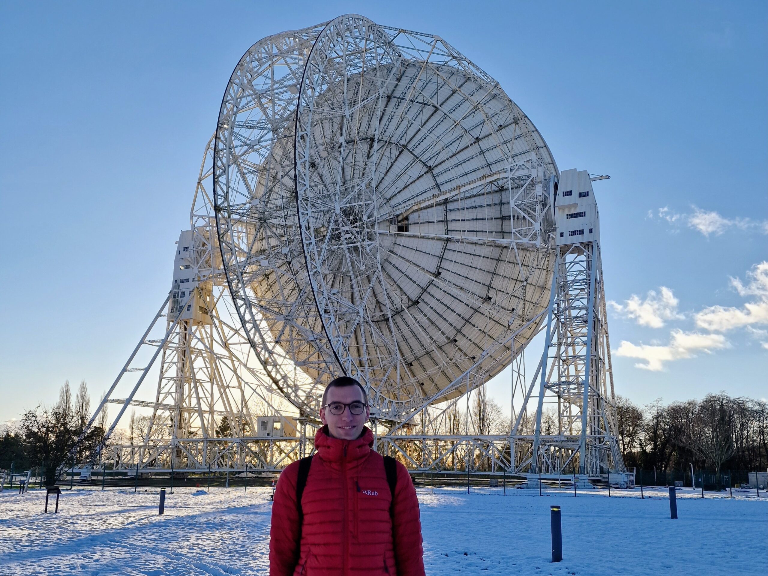 Man in a red jacket in the snow in front of a large telescope