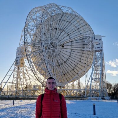 Mann in roter Jacke im Schnee vor einem großen Teleskop