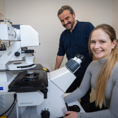 Zwei Personen mit einem großen Mikroskop.