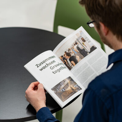Man leafing through a print magazine, eye-catching headline in the magazine: Growing together