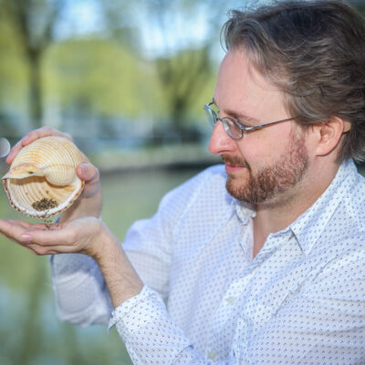 Mann hät ein großes Schneckenhaus in der Hand aus dem kleine Scheckenhäuser rieseln.