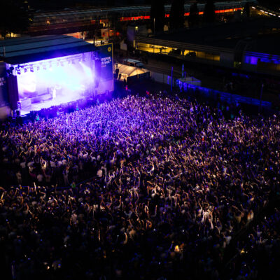 luftaufnahme eines Festivalgeländes: Eine große Menschenmenge stehen eng vor der Bühneund hört Musik.