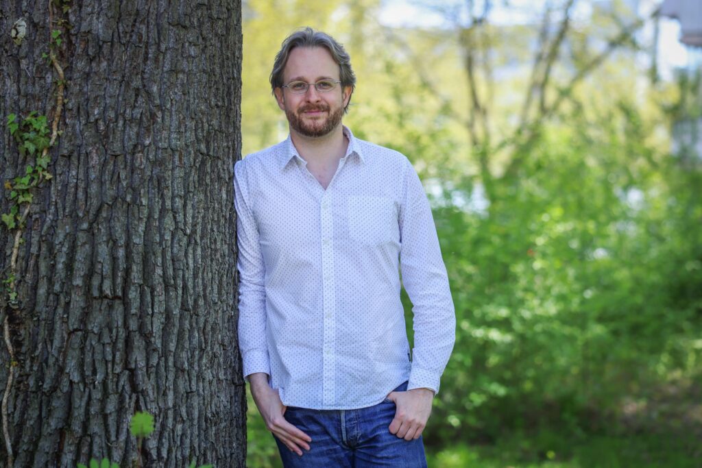 Ein Mann lehnt bei Sonnenschein an einem Baum