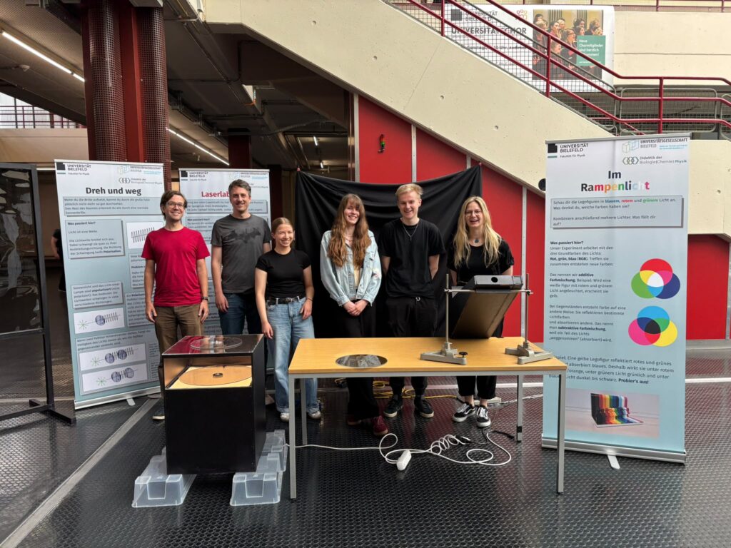 Studierende und eine Lehrende präsentiere ihre Physik-Ausstellung in der Uni-Halle der Universität. 