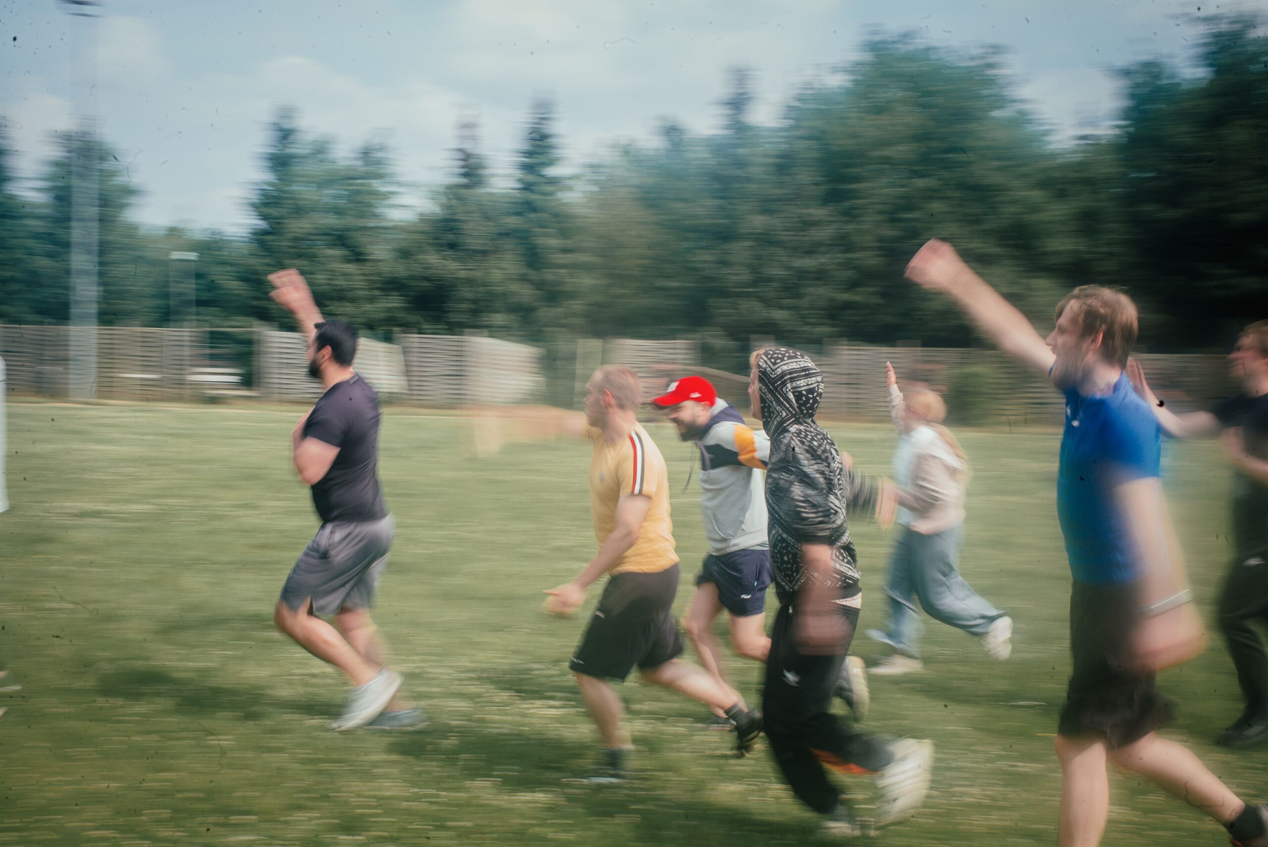 Ein verschwommenes Foto von jungen Männern in Sportkleidung, die auf einer Wiese Aufwärmübungen machen.