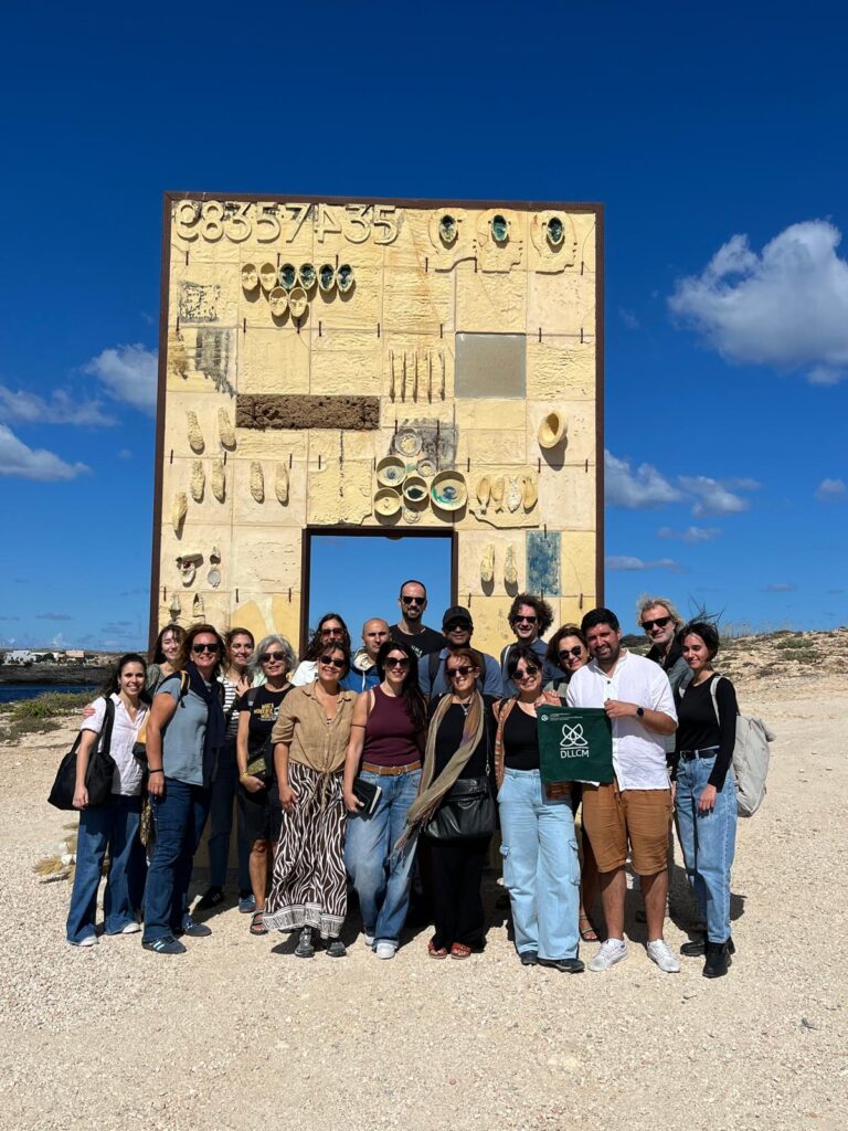 Ein Gruppenfoto von Wissenschaftler*innen in Lampedusa vor dem Denkmal.