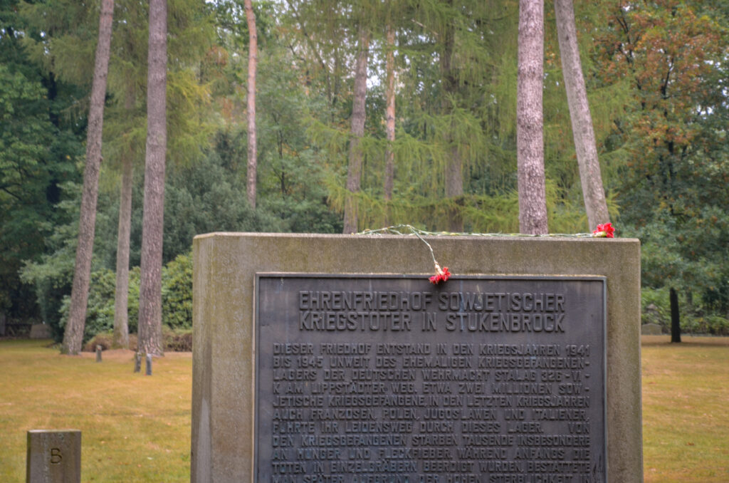 Foto eines Steins mit Inschrift auf dem Sowjetischen Ehrenfriedhof in Schloss Holte-Stukenbrock. Auf dem Stein liegt eine rote Blume.