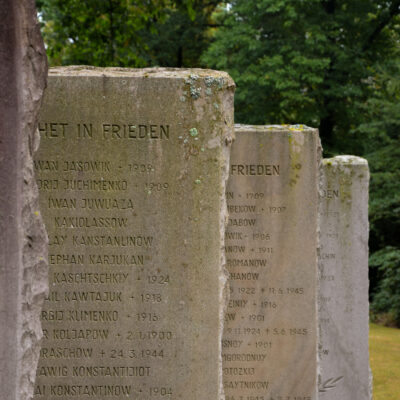 Ein Foto von drei Steintafeln mit der Aufschrift „Ruhet in Frieden“ und den Namen von Personen, die im Lager Stalag 326 interniert waren.